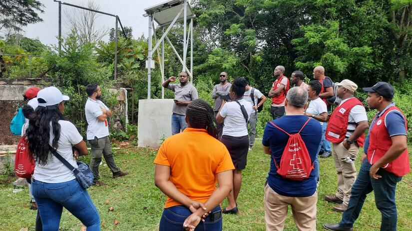 Personal y voluntariado de la Cruz Roja de todo el Caribe escuchan a representantes de Konnexx Services Ltd. explicar cómo funciona la bomba de agua solar (al fondo), durante una visita de campo al Centro Cristiano Caribeño para Personas Sordas (CCCD).