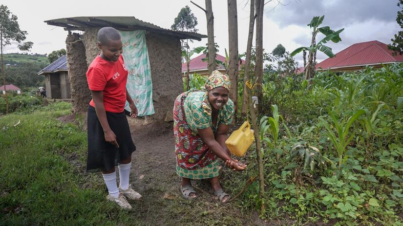 Kikanshemeza watches and smiles as her mother washes her hands using a tippy tap she built at home.