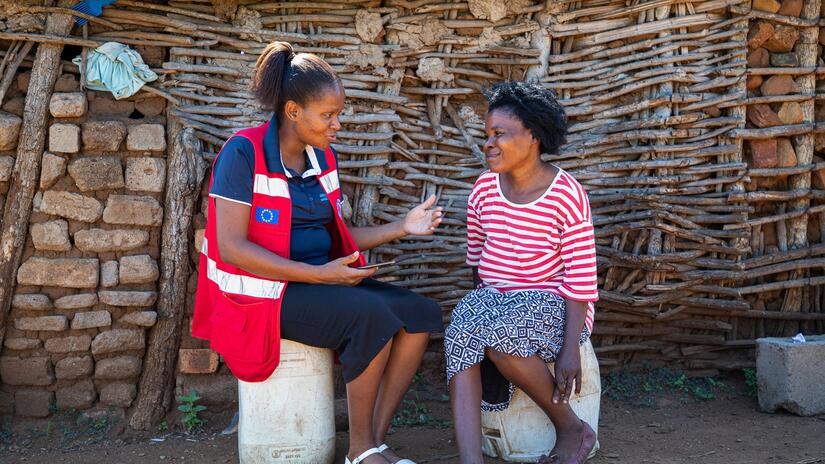 Baphalali Eswatini Red Cross Society volunteer Bethusile Nxumalo speaks with 44-year-old Winile Masuku outside her home.