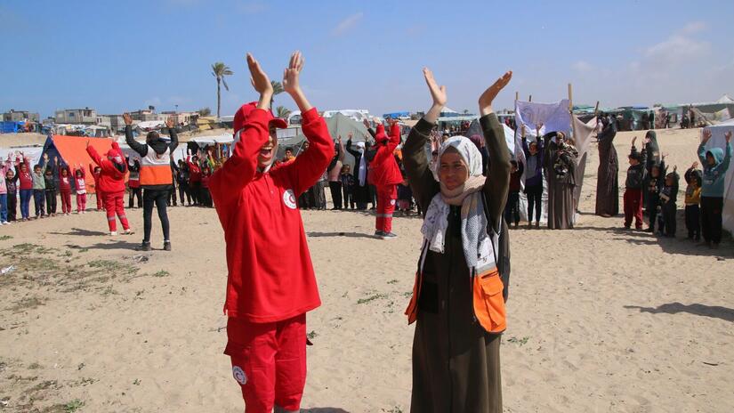 احدى اعضاء فريق الدعم النفسي والاجتماعي التابع للهلال الأحمر الفلسطيني (على اليمين) الى جانب متطوعة في الهلال الأحمر المصري خلال نشاط ترفيهي للأطفال النازحين في رفح، غزة. 