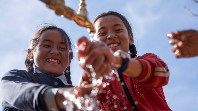 Two young children smile and laugh as they wash their hands in a newly built water tap in their village in rural Nepal.