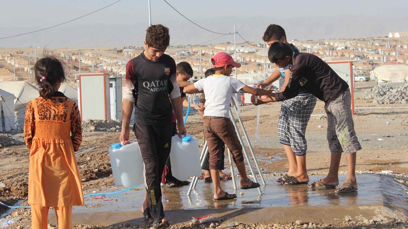Las personas afectadas por crisis son especialmente vulnerables al calor extremo. Un Un grupo de niñes iraquíes tuvieron que desplazarse a causa del conflicto. Se reúnen en torno a grifos de agua en un campamento de personas desplazadas internamente para refrescarse y llenar sus jarras de agua.