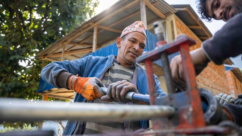 اثنان من أفراد المجتمع المحلي يقومان بتركيب الأنابيب لبئر جديد، وحوض لتجميع المياه، ونقطة توزيع المياه في قريتهم النيبالية النائية. 
