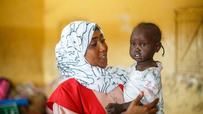 Wajdan Hassan Ahmed, volontaire du Croissant-Rouge du Soudan, tient un jeune enfant dans ses bras lors d'une visite dans un camp de personnes déplacées à Port-Soudan. 
