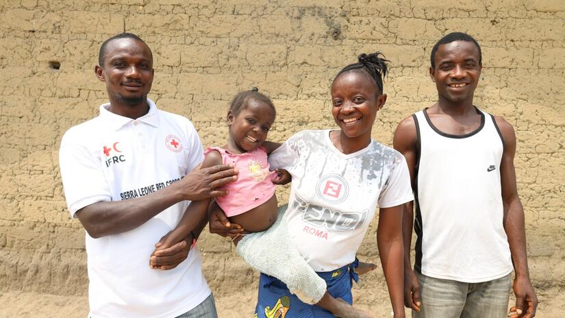 Joseph (à gauche), volontaire de la Croix-Rouge de Sierra Leone originaire de Gbaigibu, est aux côtés d'une famille qu'il a aidée à rester en bonne santé et en sécurité dans sa communauté.