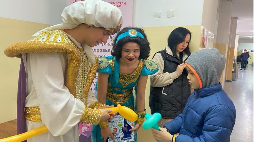 Personas voluntarias de la Media Luna Roja de Kirguistán, junto con animadores, hacen animales con globos para niñas y niños como parte de la campaña de vacunación para combatir el brote de sarampión.