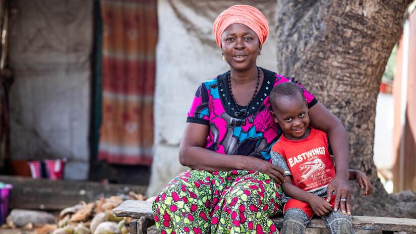 N'Mah et son jeune fils, Morlai, sont assis et sourient dans le village de Makuma au début de l'année 2024, deux ans après l'épidémie de rougeole qui a menacé leur communauté.