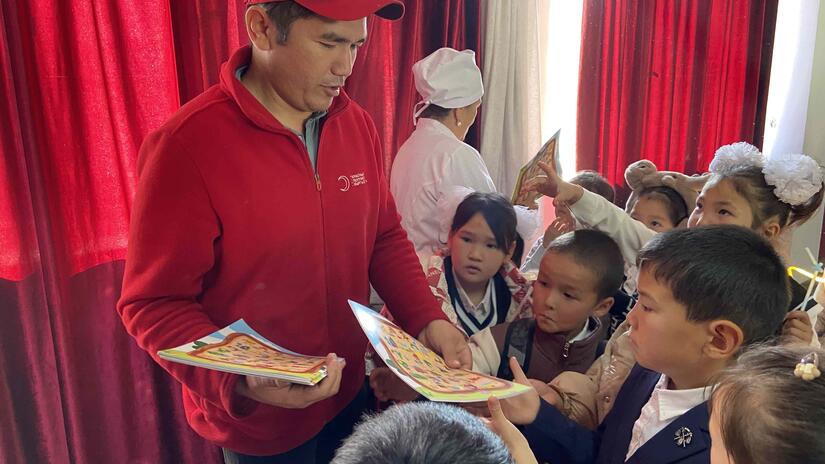Un volontaire du Croissant-Rouge du Kirghizistan distribue des bandes dessinées aux enfants vaccinés contre la rougeole.