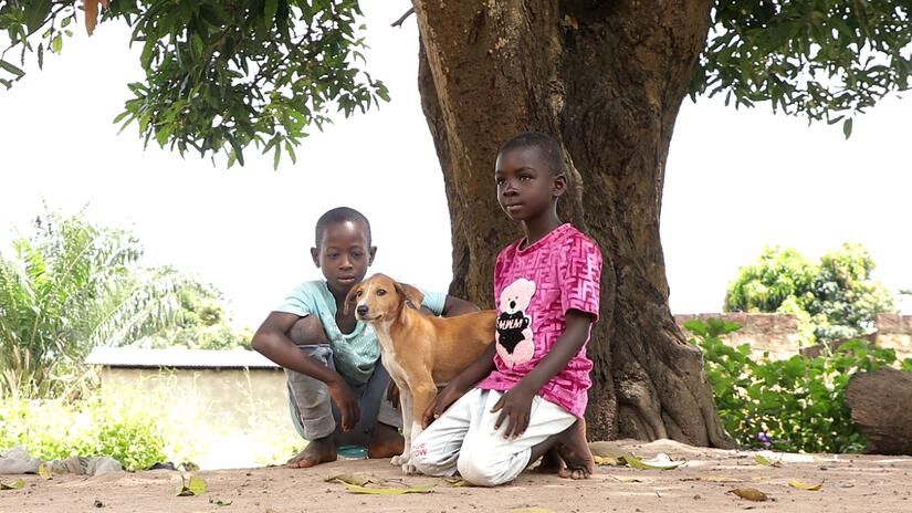 Two young boys in Faranah play together with their pet dog.