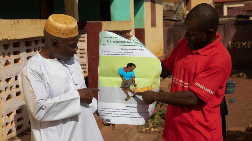 Mamadi Fofana (left) from Faranah points to a poster about rabies presented by local Guinea Red Cross volunteer, Lancinet Conde.