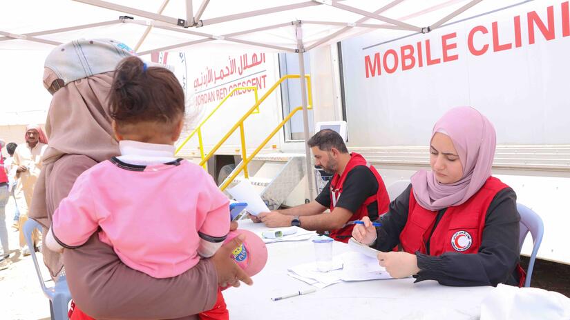 A woman and her child receive medical assistance from a Jordan Red Crescent mobile health clinic in Al-Lubban camp