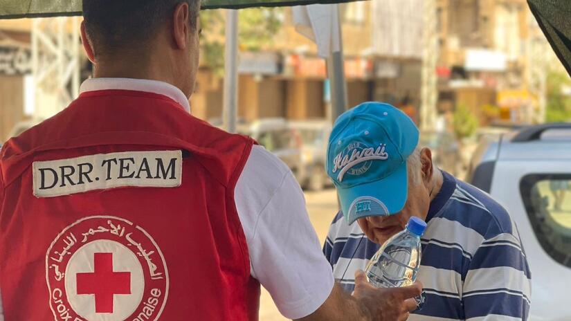 Un membre de l'équipe de réduction des risques de catastrophe de la Croix-Rouge libanaise partage une bouteille d'eau avec un homme âgé, dans le cadre d'un plan global visant à anticiper la saison des canicules.