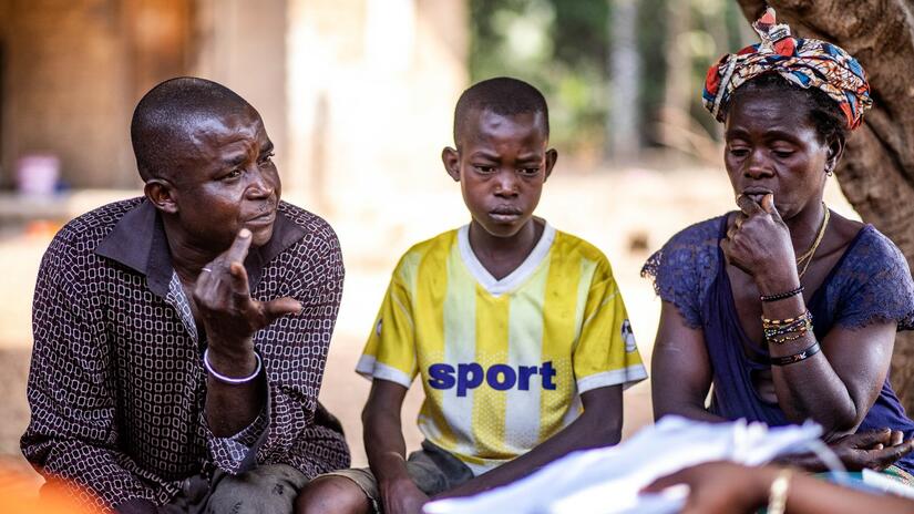 Abu sits with his parents, Saido and Mabinti, as they talk to Red Cross volunteers about his journey to proper diagnosis.