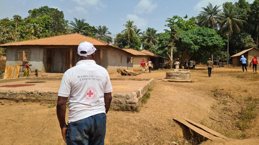 A Sierra Leone Red Cross Society volunteer in Laya Dee looks on as a community meeting is held in the shade of a tree in Laya Dee village.
