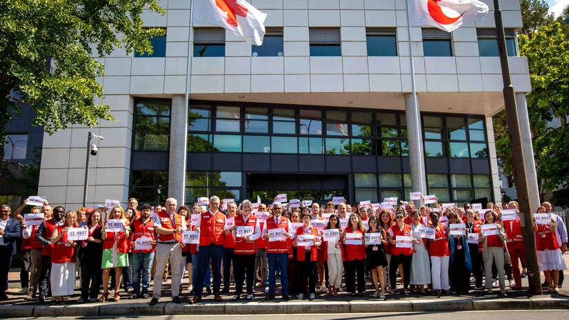 IFRC staff gather outside their headquarters in Geneva, Switzerland, holding signs saying 'We must Protect Humanity' as part of a global 'Stand in Solidarity' event demanding protection for humanitarian workers and volunteers.