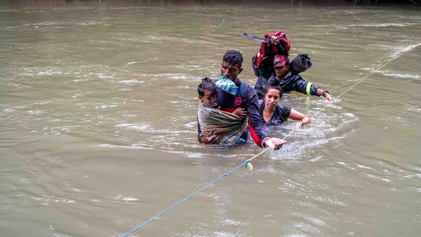 Un grupo de migrantes atraviesa un río mientras se agarran a un cable que les guía y les ayuda a mantener el rumbo a pesar de la corriente.