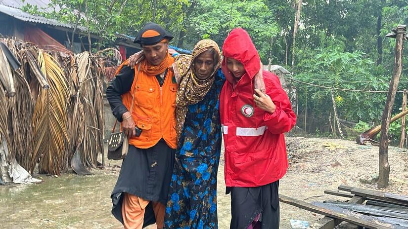 A Bangladesh Red Crescent volunteer helps a lady away from her flooded home following Cyclone Remal. The response was part funded through an IFRC-DREF allocation