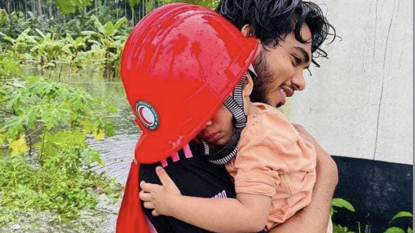 A Bangladesh Red Crescent volunteer carries a tired toddler through flood waters to safety.
