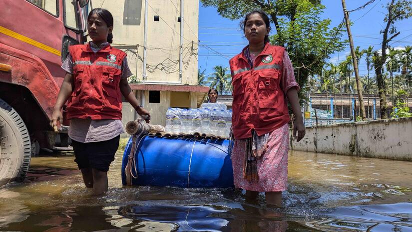 Two Bangladesh Red Crescent volunteers use a flotation device to carry cases of bottled water to people impacted by sudden, severe flooding.