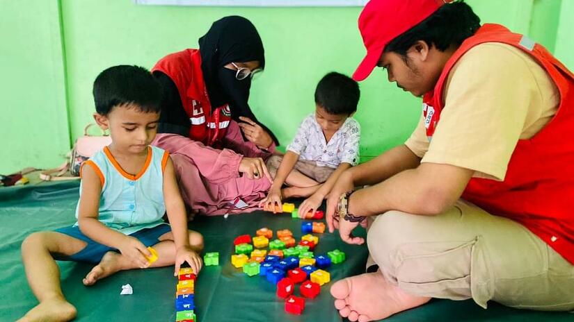 Two volunteers with the Bangladesh Red Crescent play games with two children to help take their minds off the stress of losing their homes.