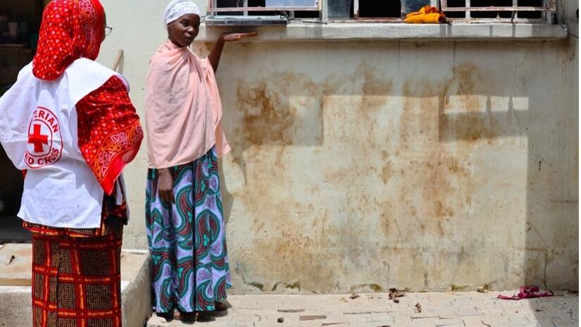 Debout devant sa maison, Hadjara Habu, mère de cinq enfants, place sa main sur le rebord d'une fenêtre, au-dessus de son épaule gauche, pour montrer la hauteur atteinte par l'eau lors des récentes inondations.