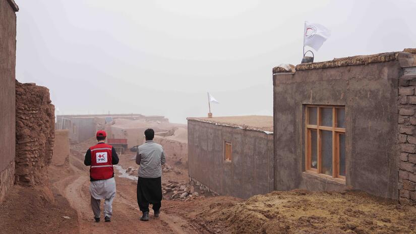 An IFRC staff member walks with a local resident among new homes built by the IFRC, the Afghan Red Crescent and other partners in the wake of devastating earthquakes in October 2023.