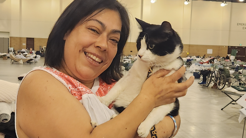 Blanca Pérez sonríe y abraza a un gato en una de las grandes salas utilizadas como refugio temporal en el Centro de Convenciones de Pasadena. Pérez perdió su casa y su tienda de ropa a causa de los incendios, pero encuentra consuelo en la compasión y el apoyo mostrados por el voluntariado de la Cruz Roja.