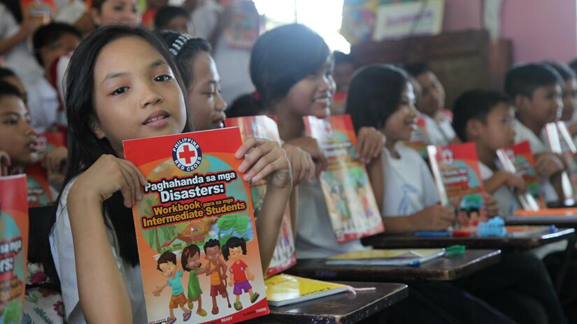 A young girl holds up a workbook that she used as part of a disaster risk reduction education program at the Santulan Elementary School near the capital of Manila in the Philippines.