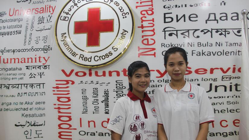 Cho Cho Aye y Phu Ngon Wai ante un muro en el que aparecen palabras que representan los principios, valores y actividades humanitarias clave de la Cruz Roja de Myanmar.