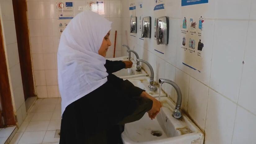 تغسل الطالبة أليف عقبة يديها بمياه نظيفة وآمنة في مدرسة أسماء للبنات بمدينة ذمار، اليمن، بفضل مشروع نفذه الهلال الأحمر اليمني، بدعم من الاتحاد الدولي لجمعيات الصليب الأحمر والهلال الأحمر والاتحاد الأوروبي.