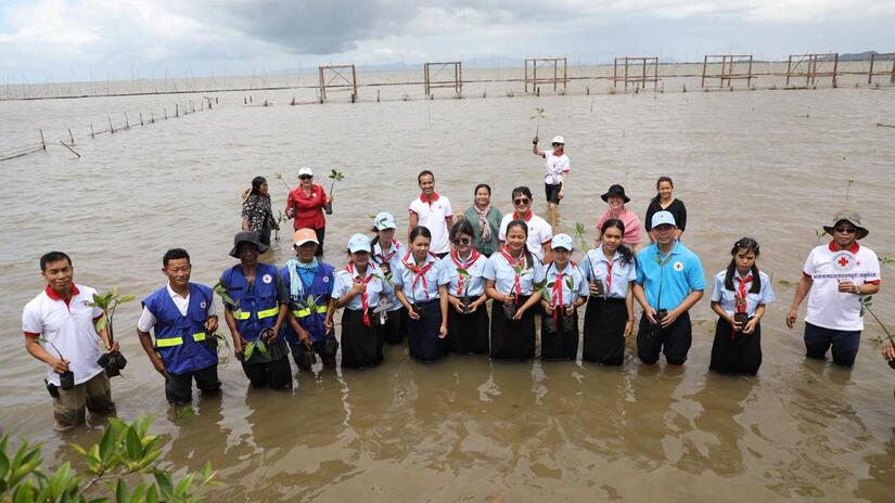 Participants in a recent mangrove planting in Kampot, Cambodia, gather for a group photo while standing knee deep in coastal waters.