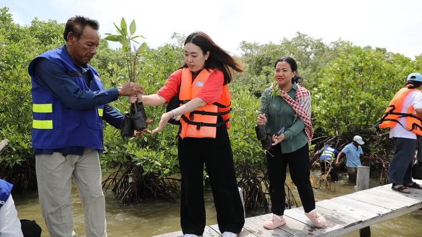 An IFRC staff member hands a sapling mangrove plant to a volunteer from the local community as they bring the young trees to the shoreline for planting.    