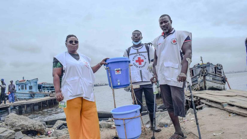 Volunteers from the Cote d’Ivoire Red Cross stand by a hand-washing station they installed on the shoreline where people take ferries across a lagoon not far from the country’s capital Abidjan.