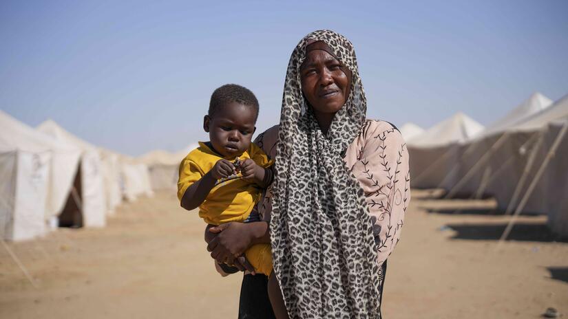 A woman stands holding her child at the Alnahda Camp in Sudan’s River Nile state, where thousands of people living in tents after fleeing their homes becuase of the ongoing conflict.  