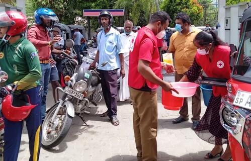 Sri Lankan Red Cross Society volunteers distribute soft drinks and snacks to people waiting in long queues at fuel stations in late May 2022