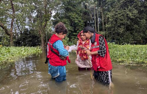 Bangladesh Red Crescent volunteers stand in water up to their waste as they provide to support to a woman living in a community impacted by heavy floods.