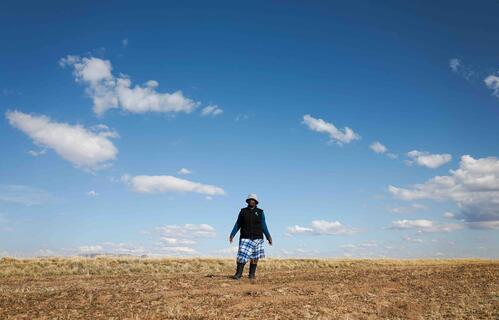 Man stands in the middle of barren field where crops were grown prior to the ongoing drought.