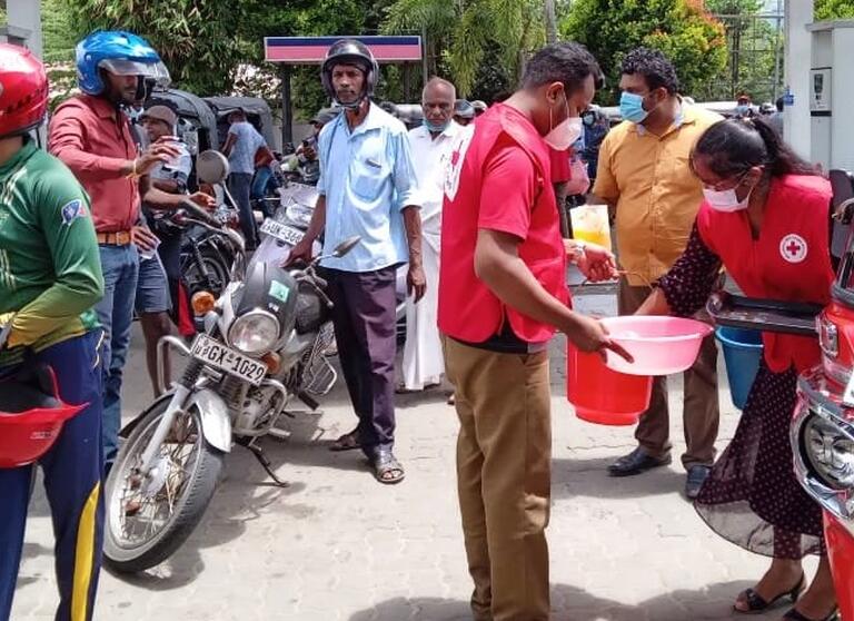 Sri Lankan Red Cross Society volunteers distribute soft drinks and snacks to people waiting in long queues at fuel stations in late May 2022
