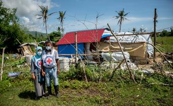 Philippine Red Cross Volunteers Nomalyn and Rene stand outside a house damaged by Typhoon Goni in late 2020