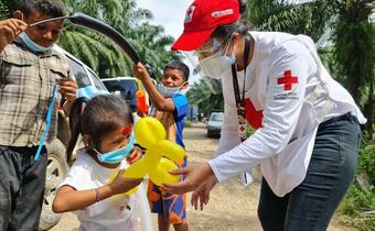 A Guatemalan Red Cross volunteer hands an inflatable balloon animal to a young girl forced to move with her family following Hurricane Eta