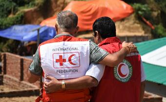 An IFRC staff member and volunteer from the Bangladesh Red Crescent hug each other as they walk to visit a new health centre set up in Cox's Bazar
