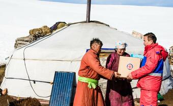 A volunteer from the Mongolia Red Cross hands a box of food and relief items to a family in Khuvzgul province to prepare for the upcoming extreme winter season