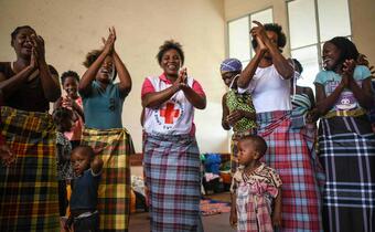 A volunteer with the Mozambique Red Cross smiling and clapping with women and children at an accommodation centre in Beira where families received humanitarian support following Cyclone Idai