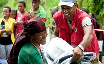 A volunteer from the Nepal Red Cross hands a self-recovery shelter kit to a woman in Lamjung district following powerful earthquakes in 2015