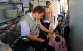 A doctor with the Syrian Arab Red Crescent performs a health check-up on a baby in a mobile health clinic during one of its regular stops near a school just south of Damascus