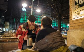 A volunteer with the German Red Cross offers a warm drink and support to a homeless person on a cold night