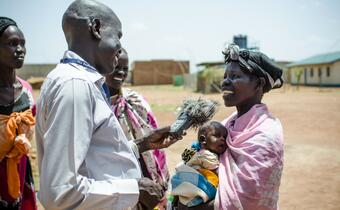A local journalist in Panemeth, South Sudan interviews a mother about receiving seeds and farming tools at a Red Cross distribution point