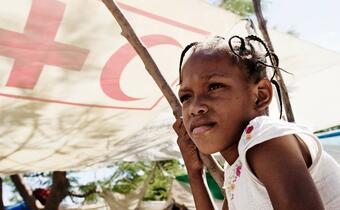 Two young girls shelter under a tarpaulin in Haiti to stay safe from strong sun and heavy rain, following the earthquake in 2010