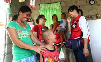 A family in Cebu, Philippines laugh and smile with Red Cross volunteers from the Japan Red Cross Society and Philippine Red Cross as they receive livelihoods assistance in 2015