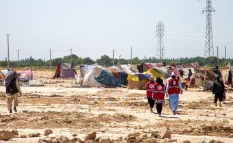 Afghan Red Crescent volunteers walk towards a small camp of internally displaced people in Balkh Province, Afghanistan in summer 2021. The Afghan Red Crescent has been delivering a cash transfer program to help people cope with multiple shocks including drought, COVID-19 and conflict.